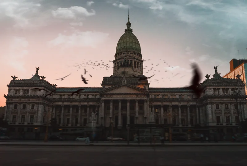 Birds flying past an ornate domed building at dusk.