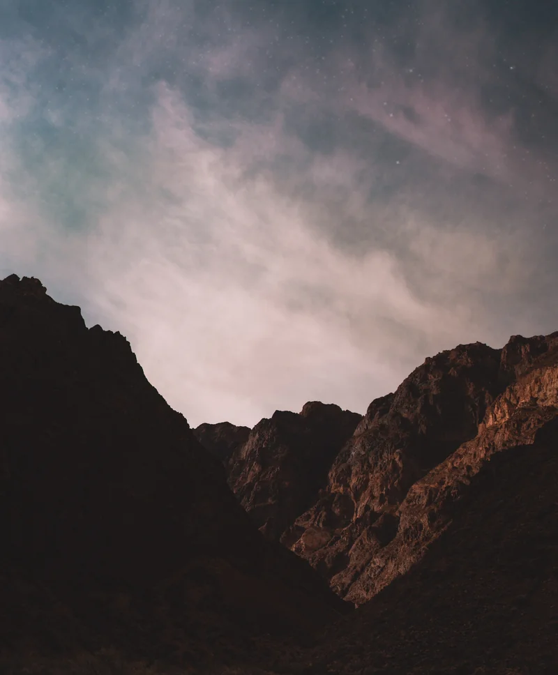Stars and soft clouds above a dark, rocky mountain landscape.